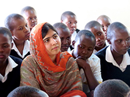 Photo of Malala Yousafzai sitting with young female students during her visit to an all-girls school in Kenya
